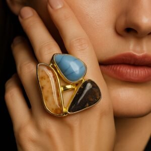 Close-up of a woman wearing a semi-precious stone ring featuring Blue Chalcedony, Dendritic Agate, and Tiger's Eye stones. The gold ring is prominently displayed on her hand, captured in soft, elegant lighting with a high-end, luxurious editorial style. avvni the store
