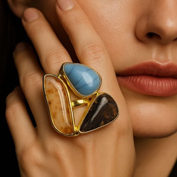 Close-up of a woman wearing a semi-precious stone ring featuring Blue Chalcedony, Dendritic Agate, and Tiger's Eye stones. The gold ring is prominently displayed on her hand, captured in soft, elegant lighting with a high-end, luxurious editorial style. avvni the store