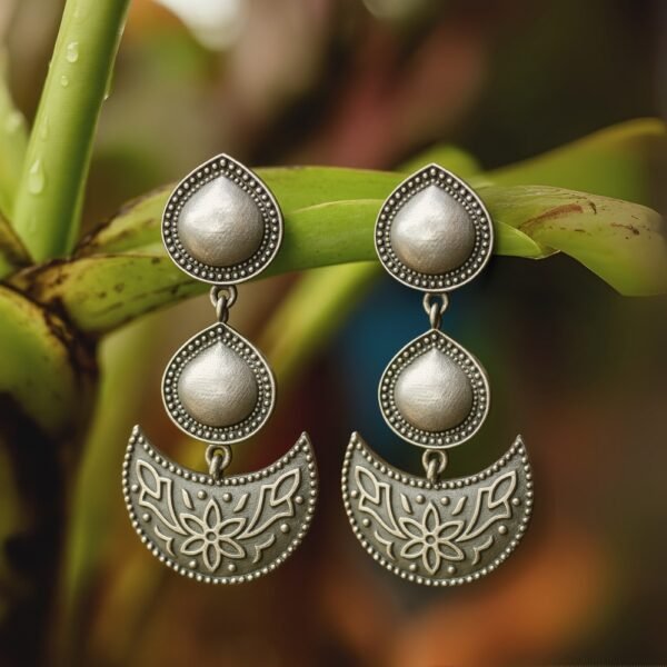 Close-up: half-moon floral pendant and teardrop domes with oxidised detailing hanging on banana tree.