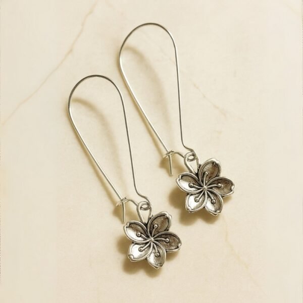 Oxidised Silver Flower Motif Dangle Earrings by Avvni Jewellery, A pair of silver flower dangle earrings with long hooks displayed on a smooth cream background.