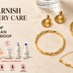 Gold anti tarnish jewellery care guide featuring shell earrings, a twisted bangle, and a wavy bar necklace on a marble background with water droplets, alongside perfume, sunscreen, lotion, and bleach to illustrate that waterproof jewellery is not chemical proof.
